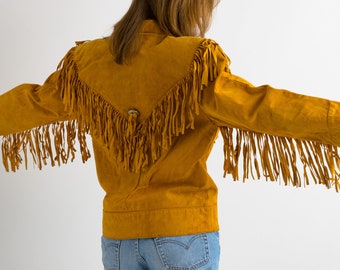 May include: A mustard yellow suede jacket with fringe detailing on the shoulders, sleeves, and back. The jacket has a button closure and a pointed collar.