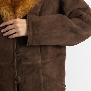 May include: A brown suede coat with a shearling collar. The coat features a button-down front and a tailored fit. The shearling collar is a warm, light brown color. The coat is a classic style, suitable for cold weather.