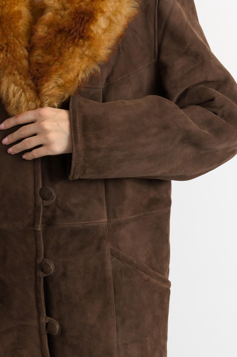 May include: A brown suede coat with a shearling collar. The coat features a button-down front and a tailored fit. The shearling collar is a warm, light brown color. The coat is a classic style, suitable for cold weather.