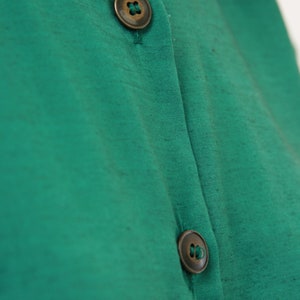Puede incluir: Una camisa verde de botones con dos botones de lat&oacute;n.
