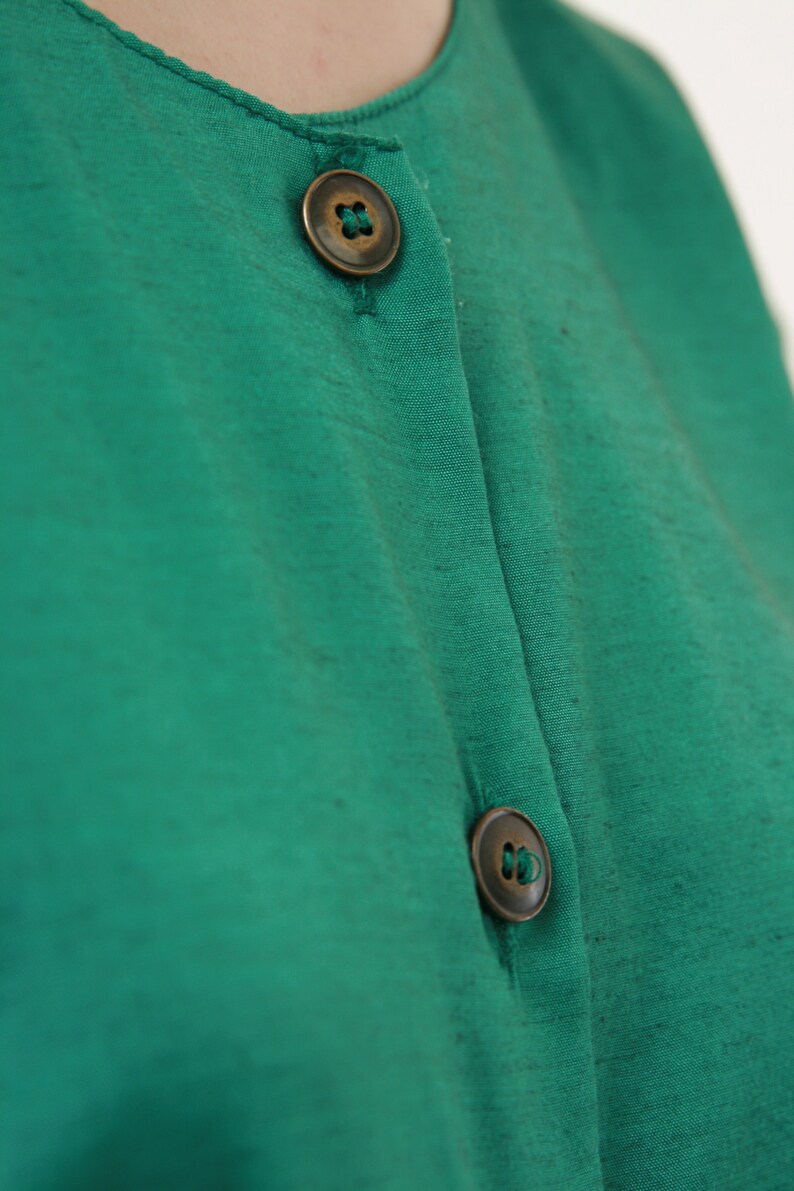 Puede incluir: Una camisa verde de botones con dos botones de lat&oacute;n.