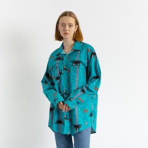 May include: A turquoise blue long-sleeved shirt with a colorful patterned design. The shirt has a button-up front and a relaxed fit.
