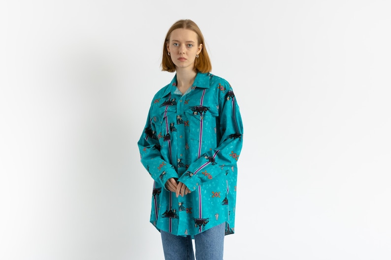 May include: A turquoise blue long-sleeved shirt with a colorful patterned design. The shirt has a button-up front and a relaxed fit.