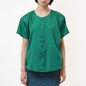 Puede incluir: Una camisa verde con botones, mangas cortas y una falda vaquera.
