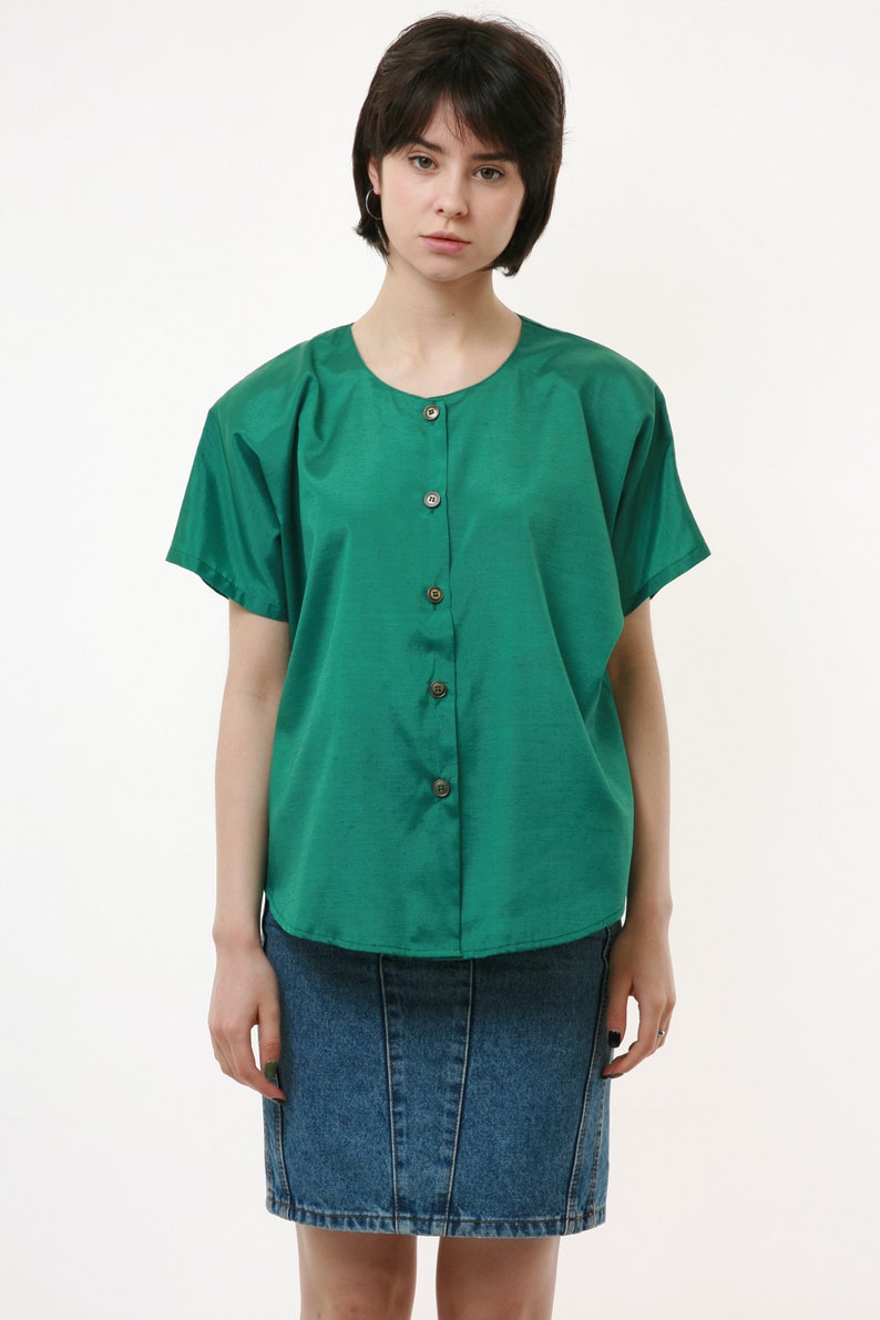 Puede incluir: Una camisa verde con botones, mangas cortas y una falda vaquera.