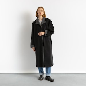 May include: A long black coat with a gray collar and cuffs. The coat is lined with a gray fabric and has a single button closure. The model is wearing blue jeans and black shoes.