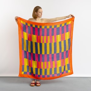 May include: A colorful geometric patterned scarf in shades of orange, yellow, pink, and blue. The scarf is made of a soft, lightweight fabric and is perfect for adding a pop of color to any outfit.