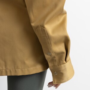 May include: A long-sleeved, tan shirt with a button-down collar and two button closures on the cuff. The shirt is made of a smooth, lightweight fabric.