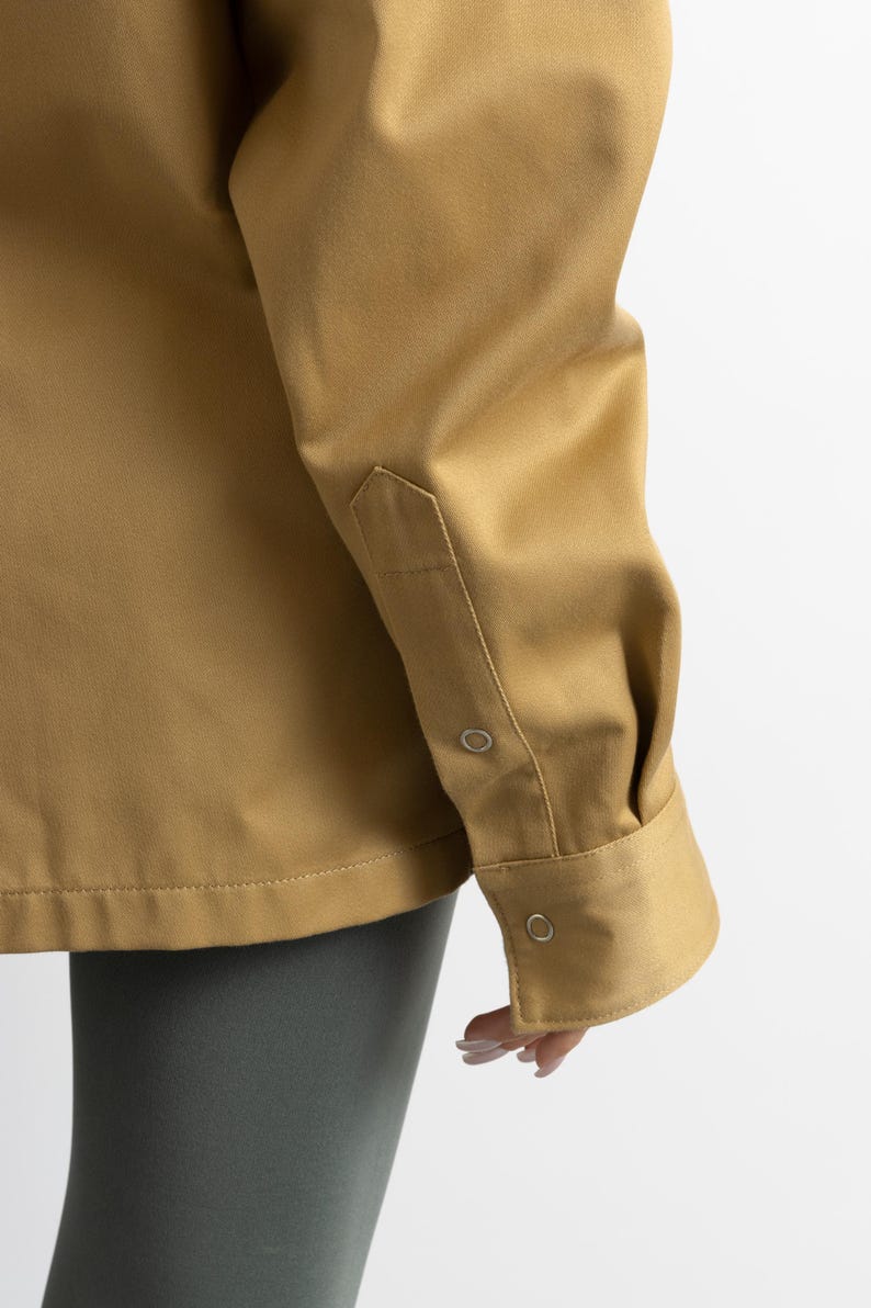May include: A long-sleeved, tan shirt with a button-down collar and two button closures on the cuff. The shirt is made of a smooth, lightweight fabric.