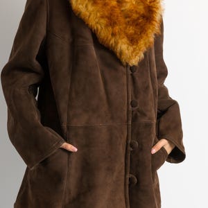 May include: A brown suede coat with a large, fluffy, tan-colored collar. The coat has a button-up front, pockets, and a classic design. The coat is a medium length and appears to be vintage.