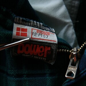 May include: A green and blue plaid jacket with a zipper closure and a Power Jeans & Jackets label. The label also includes a size tag that reads "Str/Size 22 M 67".
