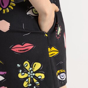 May include: A black dress with a colorful print of eyes, lips, and flowers. The dress has a pocket on the side.