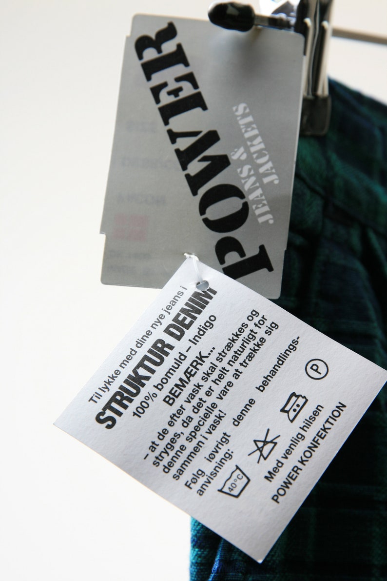 May include: A white tag with black text that reads "Til lykke med dine nye jeans i 100% bomuld - Indigo STRUKTUR DENIM BEM&AElig;RK... - at de efter vask skal str&aelig;kkes og stryges, da det er helt naturligt for denne specielle vare at tr&aelig;kke sig sammen i vask! F&oslash;lg i&oslash;vrigt denne behandlings- anvisning: 40&deg;C Med venlig hilsen POWER KONFEKTION".