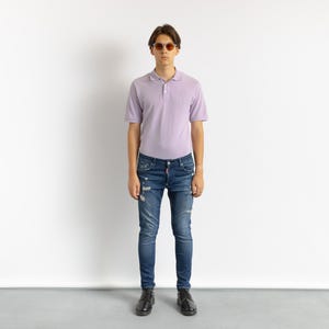 May include: A person wearing a light purple polo shirt, distressed blue jeans, black shoes, and sunglasses. The jeans have ripped details. The background is plain white.