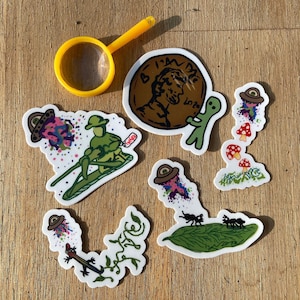 Pode incluir: Um conjunto de adesivos coloridos com vários designs, incluindo um alienígena verde segurando um centavo com o texto "I'm  Done  Loto", uma figura verde em uma prancha de surf com um OVNI acima, uma videira verde com um lagarto, uma folha com duas formigas e um grupo de cogumelos com um OVNI acima.