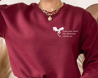 Puede incluir: Una sudadera color burdeos con un gráfico de dragón blanco y el texto "from now until the darkness claims us."