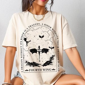 May include: A beige t-shirt with a black graphic print of a dragon and the text "A tragedy. A rider without their dragon is dead. A dragon without its rider is a fourth wing."