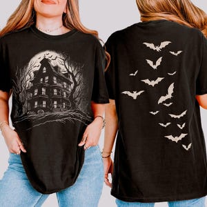 May include: Black t-shirt with a haunted house graphic on the front and a bat design on the back. The front graphic shows a spooky house under a full moon. The back of the shirt has a descending pattern of bats.
