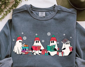 Puede incluir: Sudadera azul denim con un gráfico de cuatro fantasmas de dibujos animados que llevan gorros rojos y verdes, leyendo libros y rodeados de copos de nieve y regalos envueltos. La palabra "DENIM" está impresa en la parte inferior.