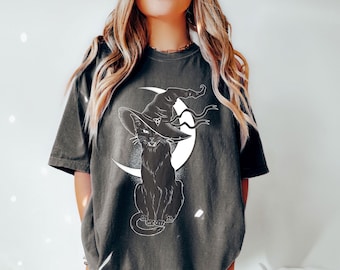 May include: A dark gray t-shirt with a black cat wearing a witch's hat and sitting on a crescent moon. The cat and moon are white.