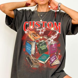 May include: A charcoal gray oversized t-shirt with a graphic print of books and lightning bolts. The text "CUSTOM" is printed in red on the front of the shirt.