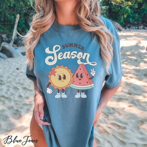 May include: A blue t-shirt with a graphic of a smiling sun and watermelon with the text "Summer Season".
