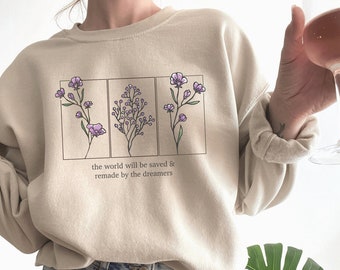 May include: A beige sweatshirt with a graphic of three floral arrangements and the text "the world will be saved & remade by the dreamers".