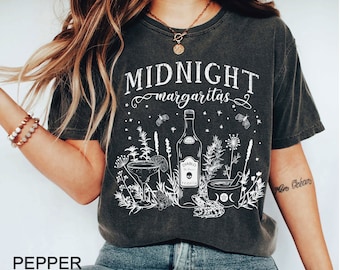 May include: A dark grey t-shirt with a white graphic design featuring a bottle of tequila, a margarita glass, and a frog. The text "MIDNIGHT margaritas" is printed on the shirt.