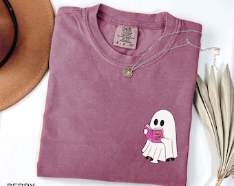 May include: A mauve colored t-shirt with a white ghost reading a book. The t-shirt has the text "COMFORT COLORS" on the tag.