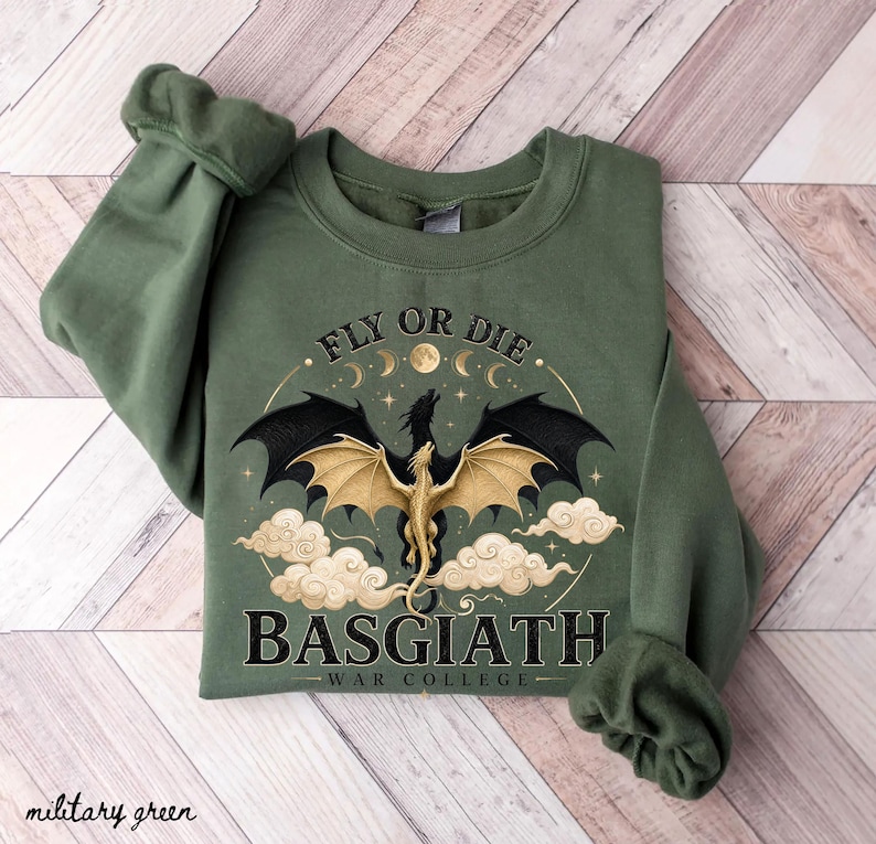 May include: Military green sweatshirt with a dragon graphic. The design features a dragon with gold wings, black wings, and the text "FLY OR DIE" and "BASGIATH WAR COLLEGE". The sweatshirt is made of a soft material.