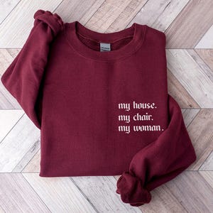 May include: Burgundy sweatshirt with the text "my house. my chair. my woman." in white.