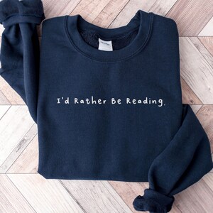 K&ouml;nnte beinhalten: Ein marineblauer Pullover mit dem Aufdruck "I'd Rather Be Reading." in wei&szlig;.