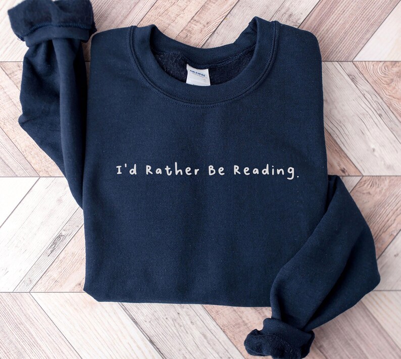 K&ouml;nnte beinhalten: Ein marineblauer Pullover mit dem Aufdruck "I'd Rather Be Reading." in wei&szlig;.