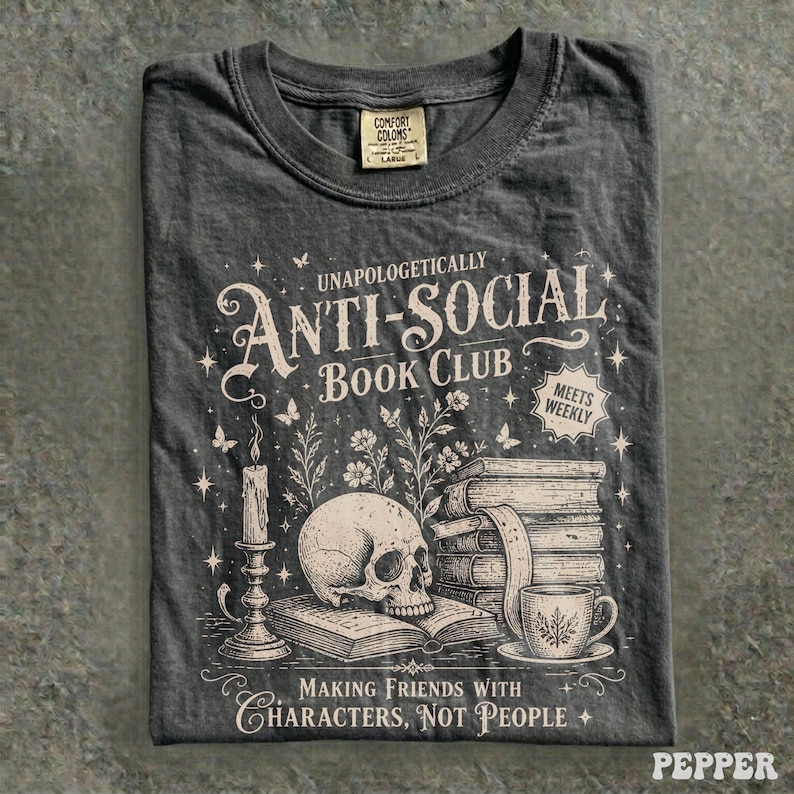 May include: Dark gray t-shirt with the text "UNAPOLOGETICALLY ANTI-SOCIAL BOOK CLUB" and a graphic of a skull, books, and a teacup. The shirt also has the text "MAKING FRIENDS WITH CHARACTERS, NOT PEOPLE".