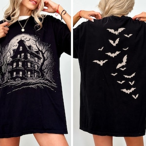 May include: Black t-shirt with a haunted house graphic on the front and a bat design on the back. The front design shows a spooky house with a full moon and bare trees. The back of the shirt has a descending pattern of bats.