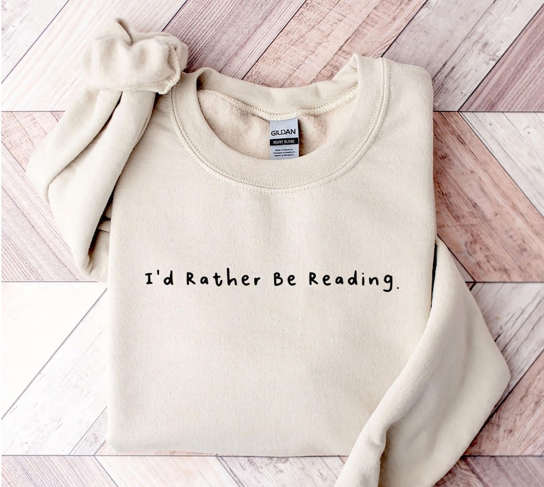 K&ouml;nnte beinhalten: Ein beiger Pullover mit dem Aufdruck "I'd Rather Be Reading." in Schwarz.