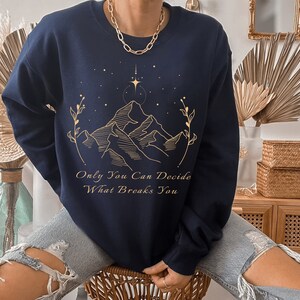 May include: Navy blue sweatshirt with a gold mountain range design and the text "Only You Can Decide What Breaks You".