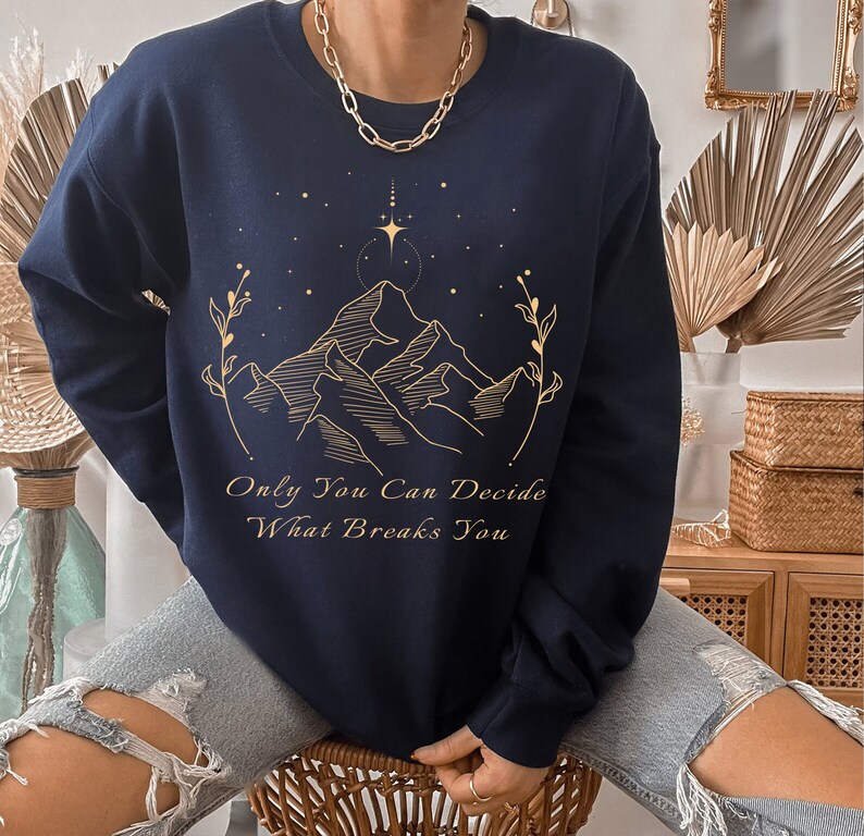 May include: Navy blue sweatshirt with a gold mountain range design and the text "Only You Can Decide What Breaks You".