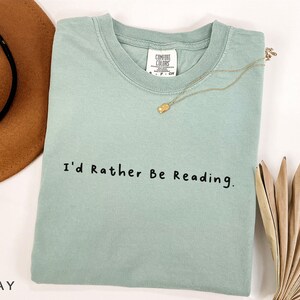 May include: A light green t-shirt with the text "I'd Rather Be Reading." printed in black.