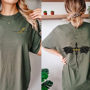 Puede incluir: Una camiseta verde con el texto "I will not die today" en la parte delantera y un drag&oacute;n negro y dorado con una luna creciente en la parte trasera.
