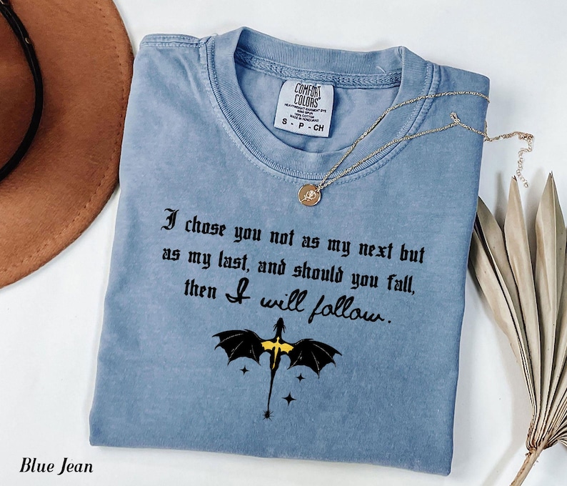 May include: A blue jean colored t-shirt with the text "I chose you not as my next but as my last, and should you fall, then I will follow." A gold necklace and a dragon graphic are also visible.