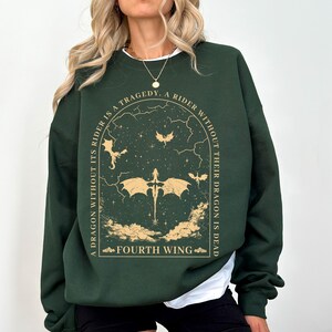 Pode incluir: Uma camisa de moletom verde escura com uma estampa gr&aacute;fica de um drag&atilde;o e o texto "A dragon without its rider is a tragedy, a rider without their dragon is dead. Fourth Wing."