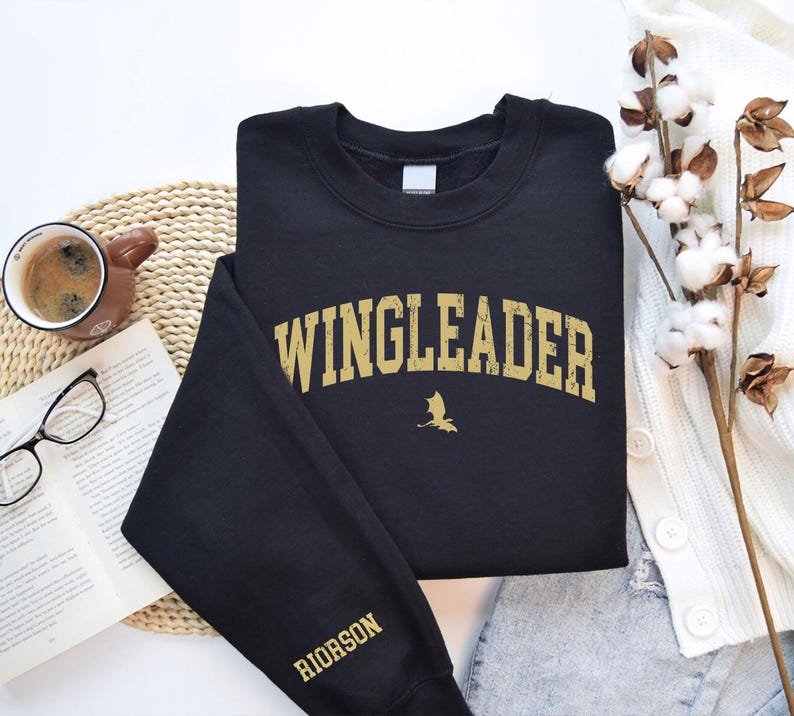 May include: Black sweatshirt with a gold graphic that says "WINGLEADER" with a small dragon silhouette underneath. The left sleeve has the word "RIORSON" in gold lettering.