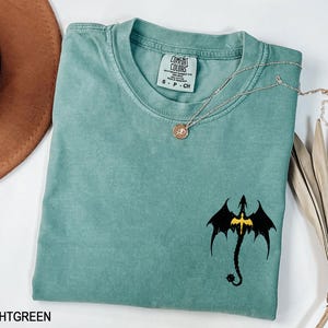 May include: Light green t-shirt with a black dragon graphic and the text "Comfort Colors" on the tag. The shirt is made of a soft, comfortable material.