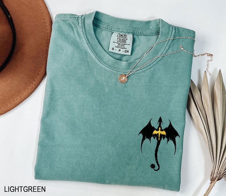May include: Light green t-shirt with a black dragon graphic and the text "Comfort Colors" on the tag. The shirt is made of a soft, comfortable material.