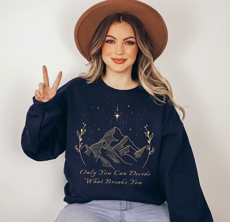 May include: A navy blue sweatshirt with a gold mountain range design and the text "Only You Can Decide What Breaks You".