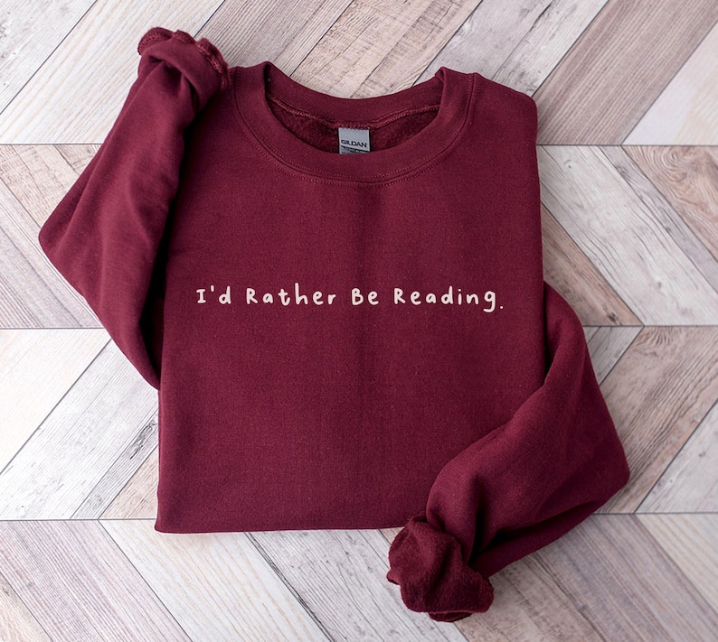 K&ouml;nnte beinhalten: Ein weinroter Pullover mit dem Text "I'd Rather Be Reading." in Wei&szlig;.