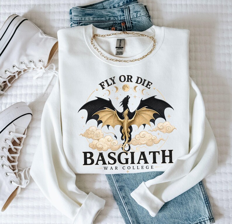 May include: White sweatshirt with a graphic of a dragon with black wings and gold accents, the text "FLY OR DIE" and "BASGIATH WAR COLLEGE". The sweatshirt is paired with blue jeans, a gold chain, and white sneakers.