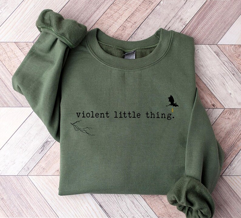 以下が含まれることがあります： 「violent little thing.」というテキストと小さな黒いドラゴンのシルエットが描かれた緑色のスウェットシャツです。