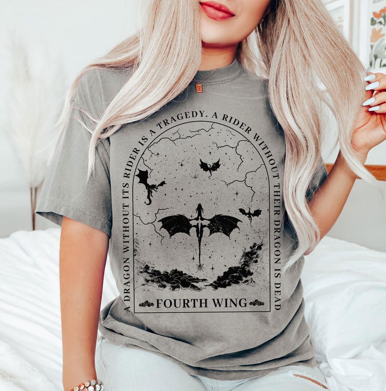 May include: A gray t-shirt with a black graphic design. The graphic features a dragon with a rider and the text "A dragon without its rider is a tragedy. A rider without their dragon is dead. Fourth Wing."